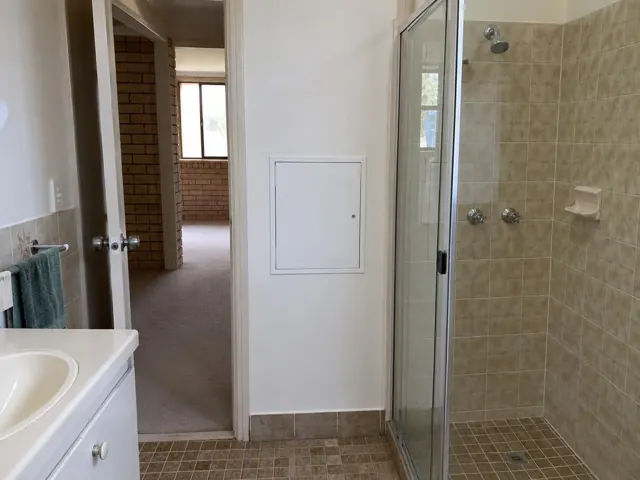 Bathroom wall with a small access panel beside a tiled shower and vanity in Meadowbank