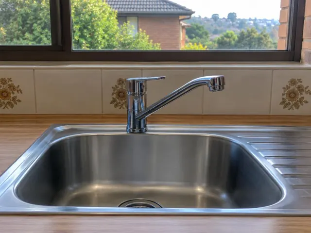 Chrome kitchen sink tap over a stainless steel sink with tiled splashback and timber bench in Meadowbank